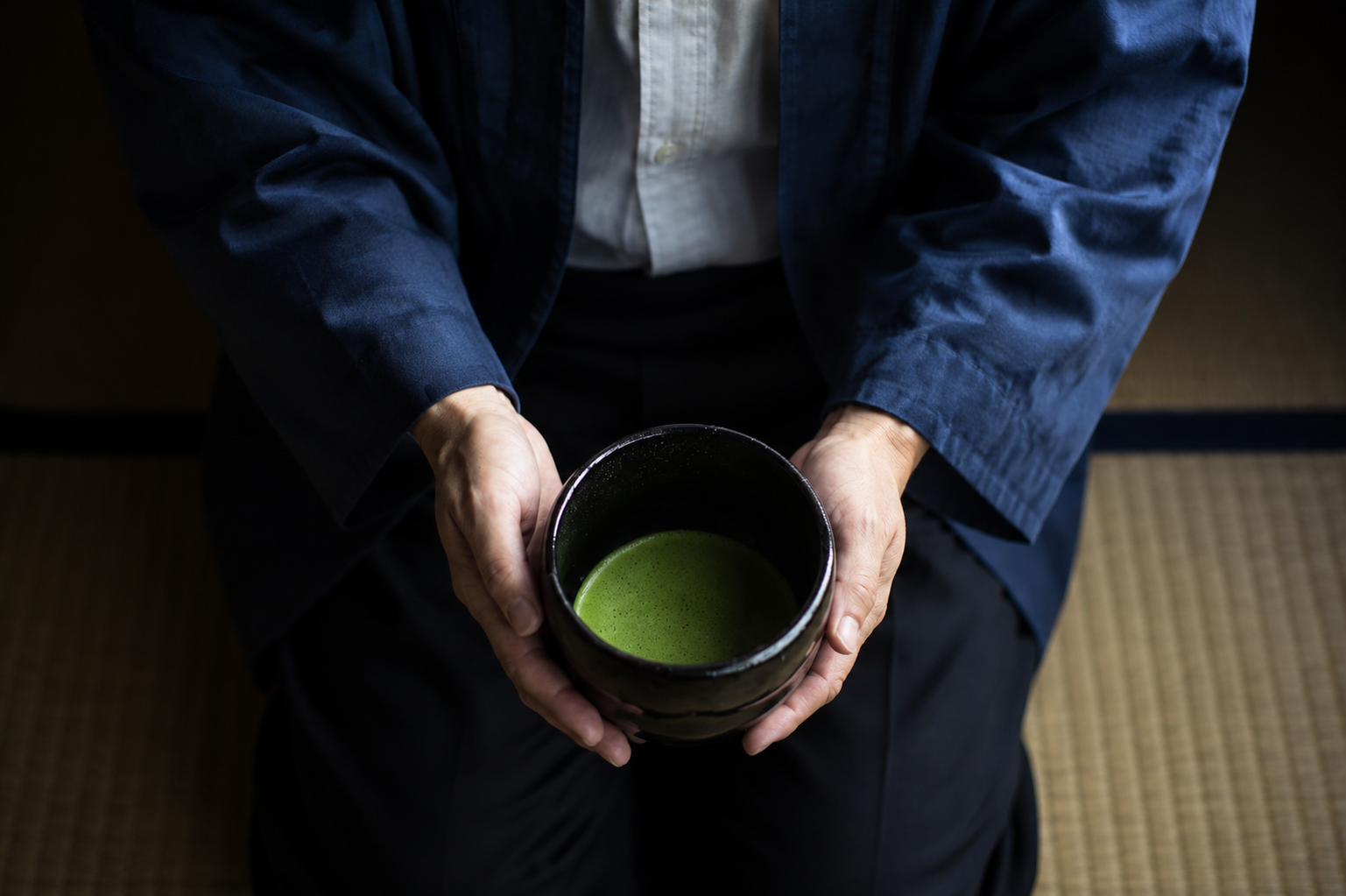 Traditional Japanese host presenting a bowl of vibrant ceremonial grade matcha during a matcha ritual.